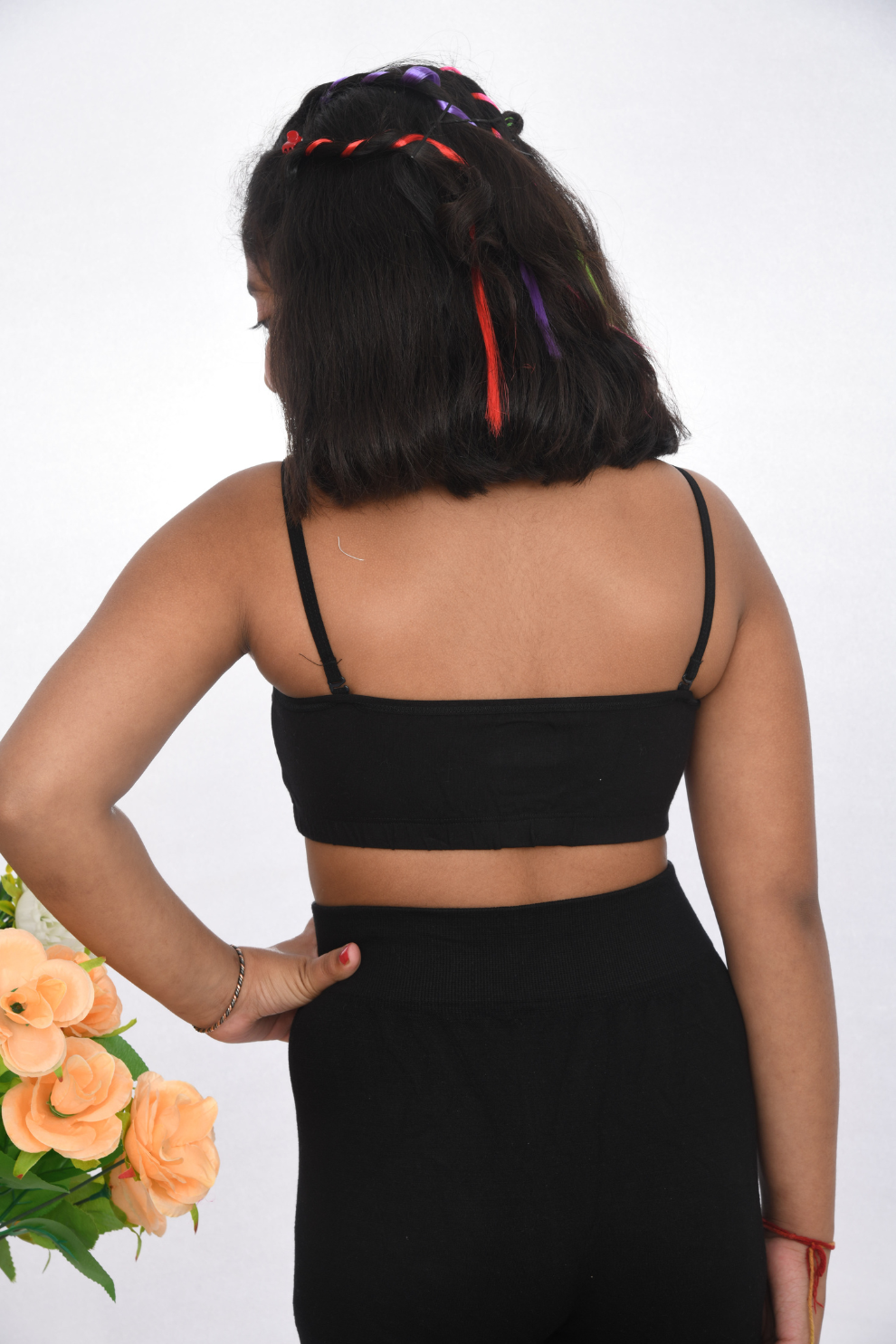 A young girl wearing a black training bra with delicate lace detailing, back view design, and adjustable straps.