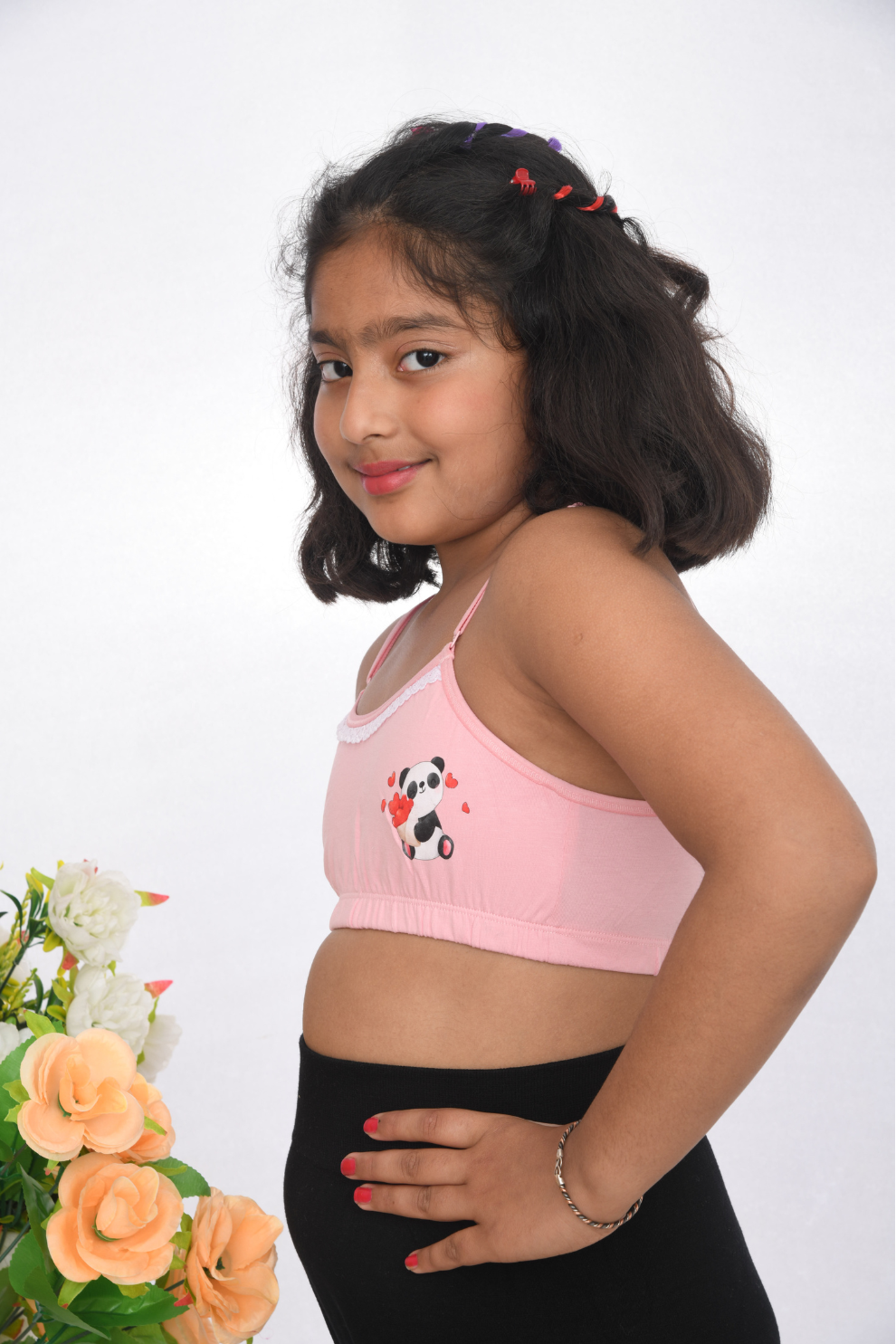 A young girl wearing a pink training bra with lace detailing, side view, adjustable straps.